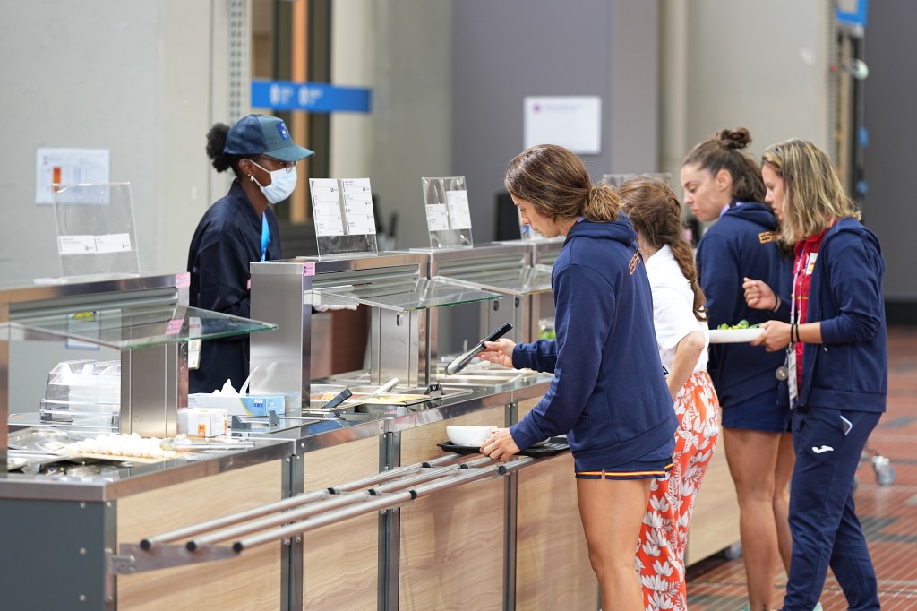 female athletes stand at the food counter in the Olympic Village